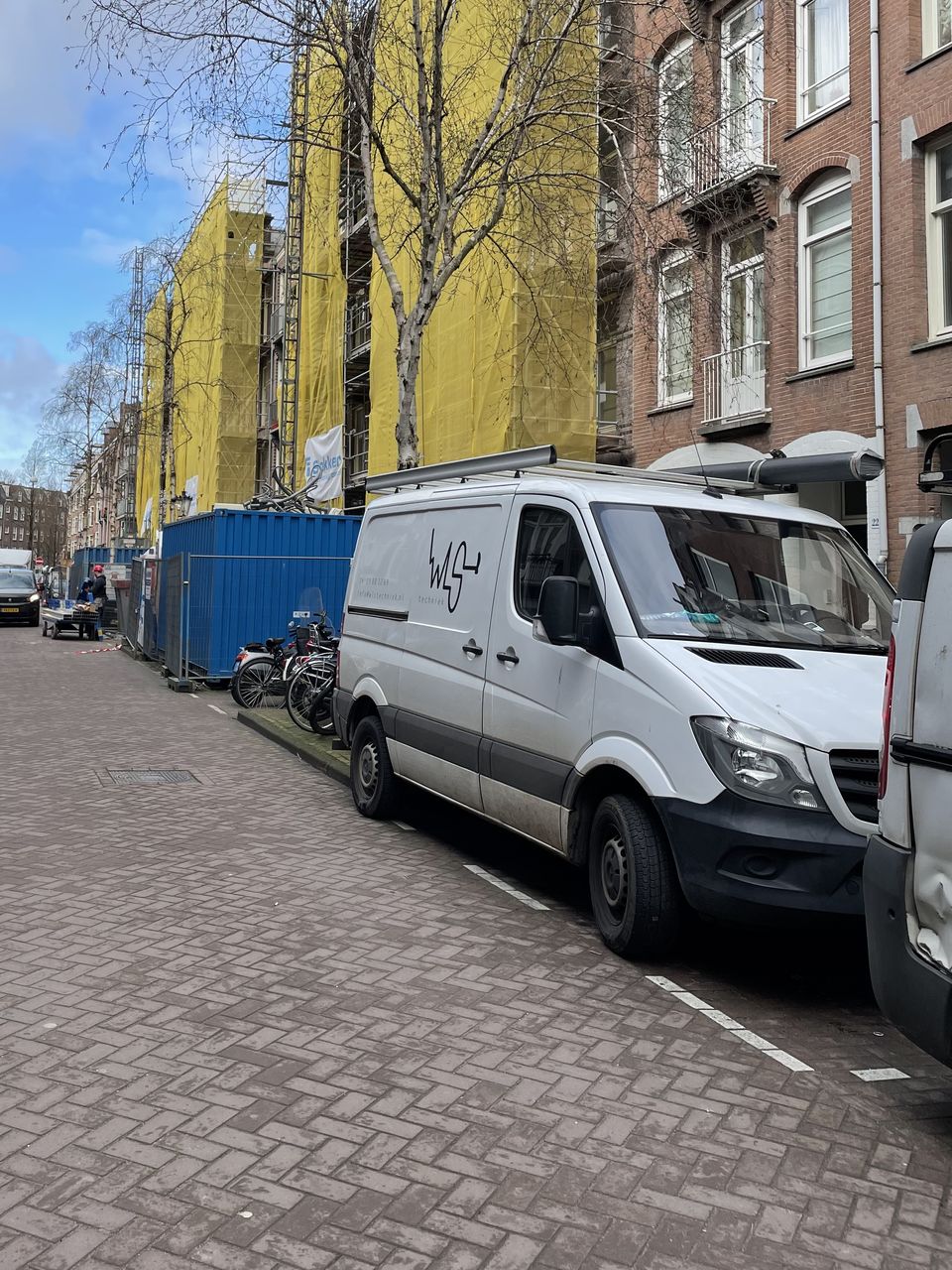 De witte bedrijfsbus van WLS Techniek met logo op de deur, geparkeerd bij een renovatieklus in de stad